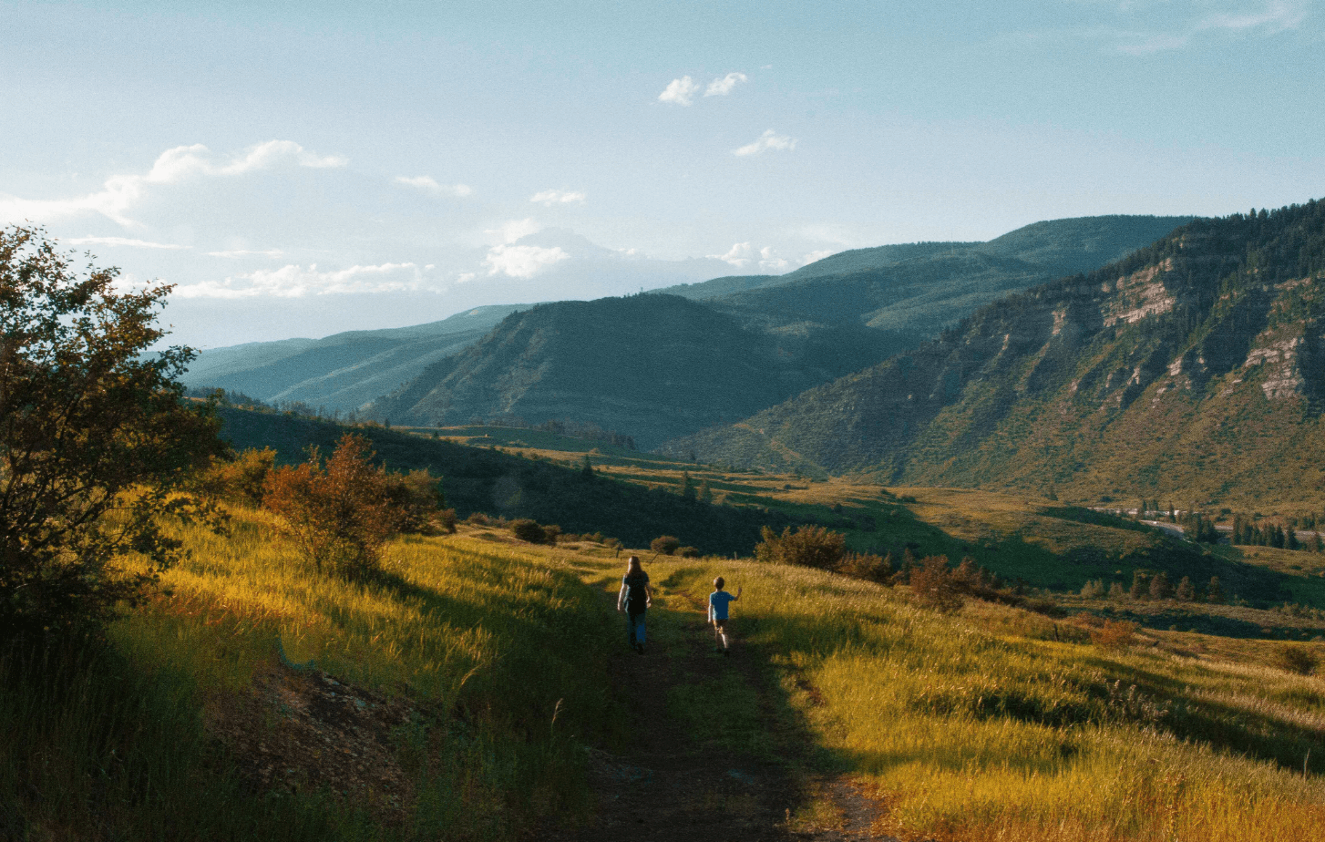 a boy and man walking on a trail on a hill at sunset